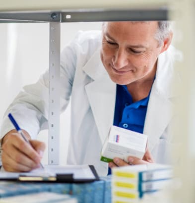 Profesional de Novaltia revisando medicamentos y registrando controles de calidad en el almacén farmacéutico.