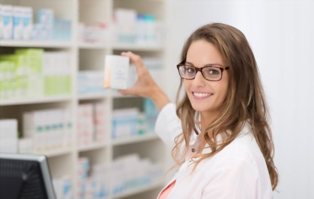 Farmacéutica de Novaltia atendiendo en la farmacia, mostrando un medicamento a los pacientes con una atención cercana.