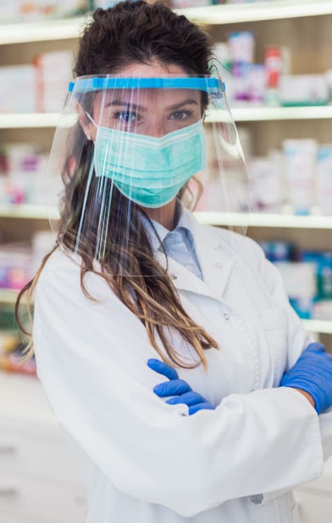 Farmacéutica en farmacia de confianza, equipada con mascarilla y pantalla de protección para atender a pacientes.